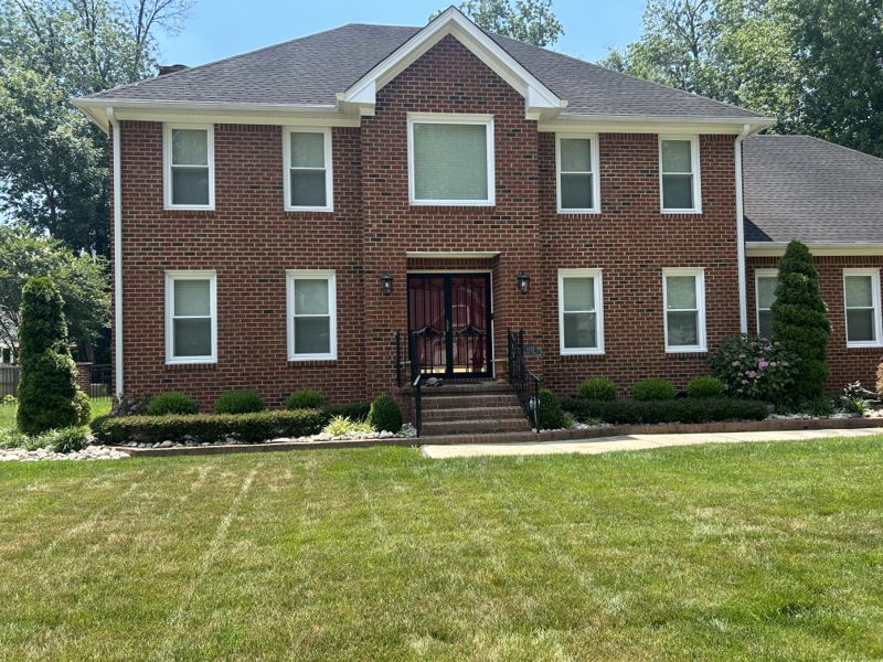 Mowed front lawn and foundation shrubs outside a two-story brick home