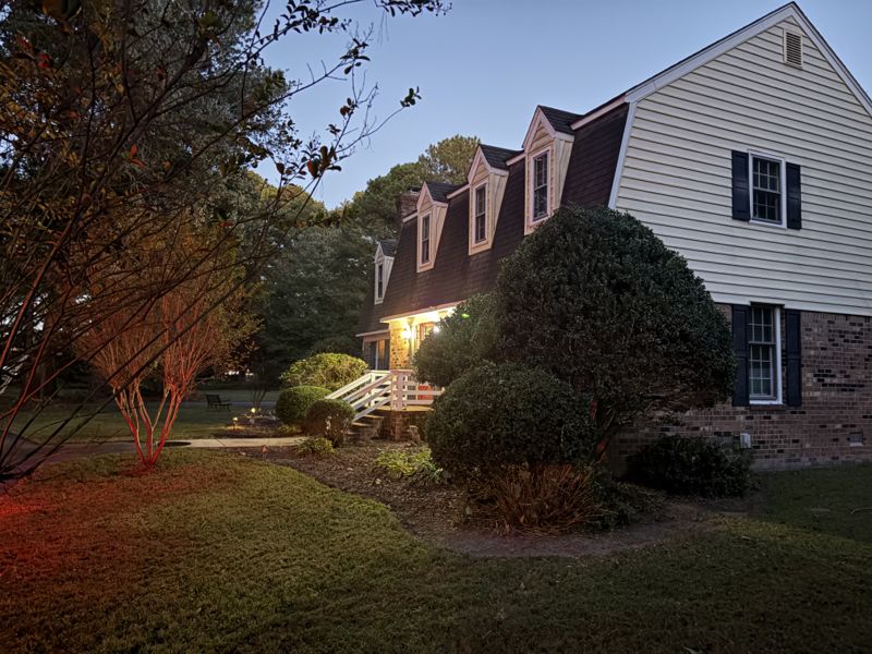 Trimmed shrubs and garden beds beside a home at dusk